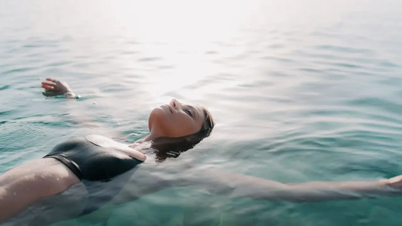 Donna galleggia sull'acqua, superando la paura di nuotare dove non si tocca. La luce del sole illumina il suo viso sereno.
