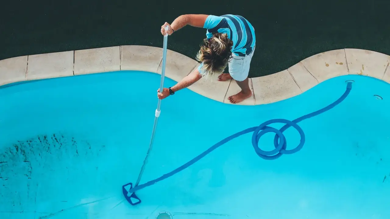 Ragazzo pulisce la piscina con un aspirafango piscina fai da te, rimuovendo detriti dal fondo azzurro.