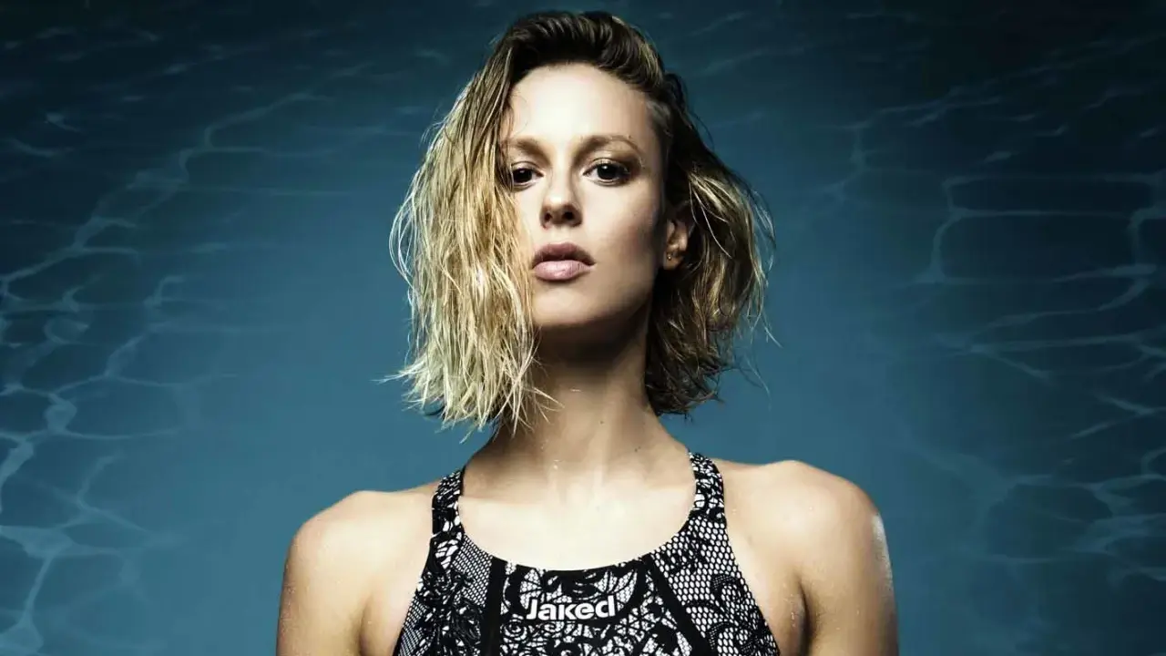 Francesca Pellegrini, nuotatrice con capelli bagnati e costume Jaked, posa con sguardo intenso su sfondo blu con riflessi d'acqua.