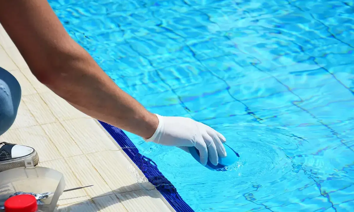 Persona con guanto bianco immerge un oggetto blu in piscina. Il cloro a cosa serve? A mantenere l'acqua pulita e sicura per nuotare.