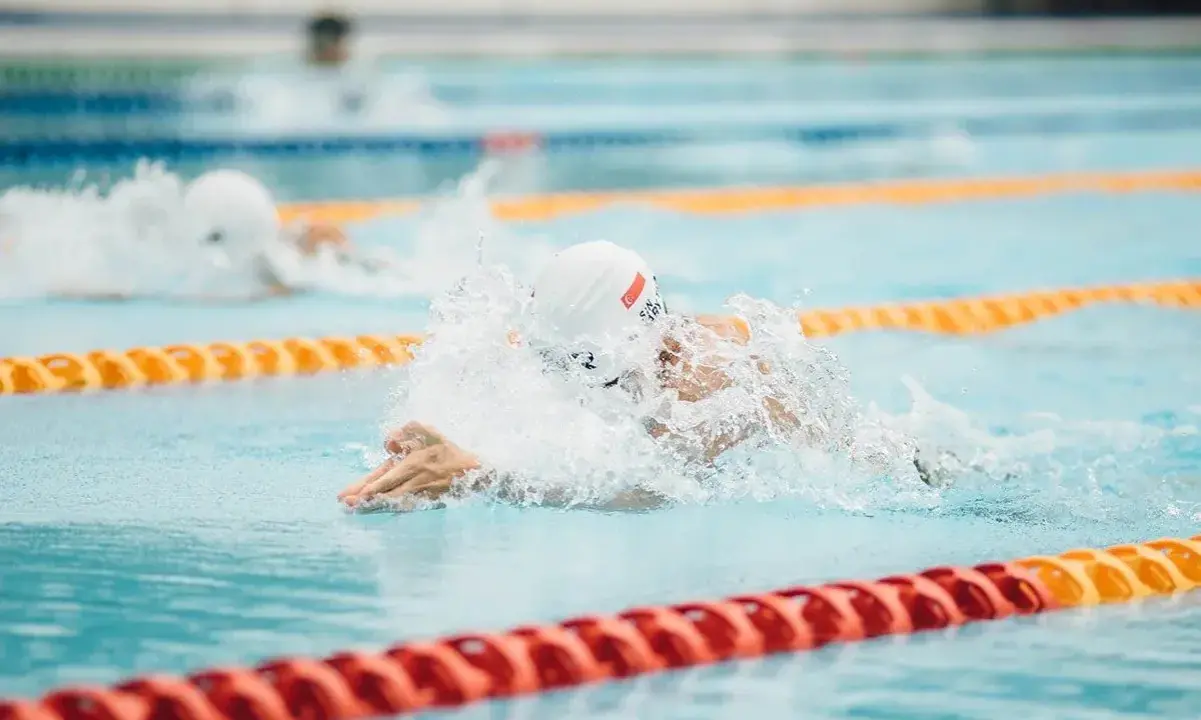 Nuotatore in azione, concentrato su come nuotare più veloce. Schizzi d'acqua e bracciate potenti in piscina.