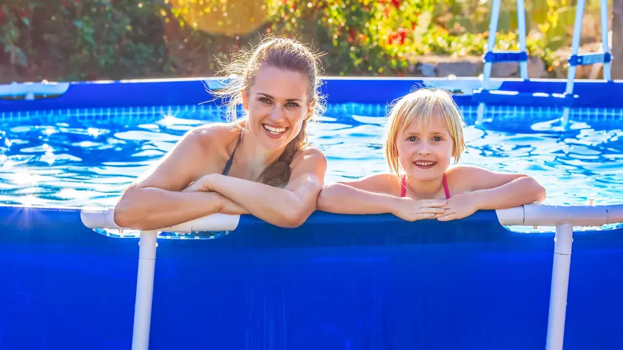 Donna e bambina sorridono in piscina. L'acqua limpida, forse trattata con bicarbonato, riflette il sole.