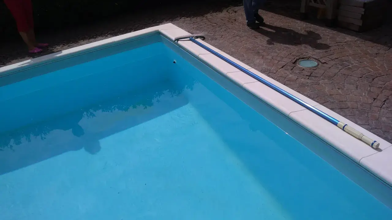 Piscina bucata: un'asta telescopica blu giace sul bordo bianco, pronta per cercare il buco.