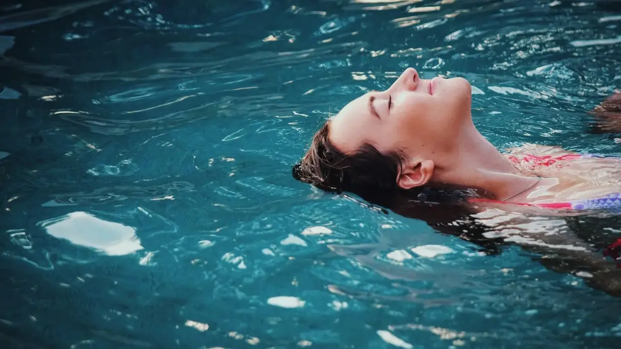 Donna galleggia serena, un passo verso come vincere la paura dell'acqua da adulti. L'acqua turchese la culla, simbolo di pace ritrovata.