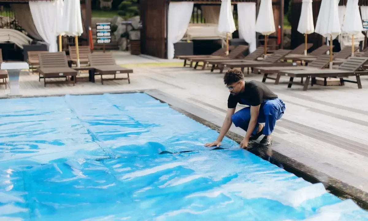 Uomo in blu sistema il telo in pvc della piscina, un passo fondamentale per capire come pulire il telo in pvc della piscina e mantenerla splendente.
