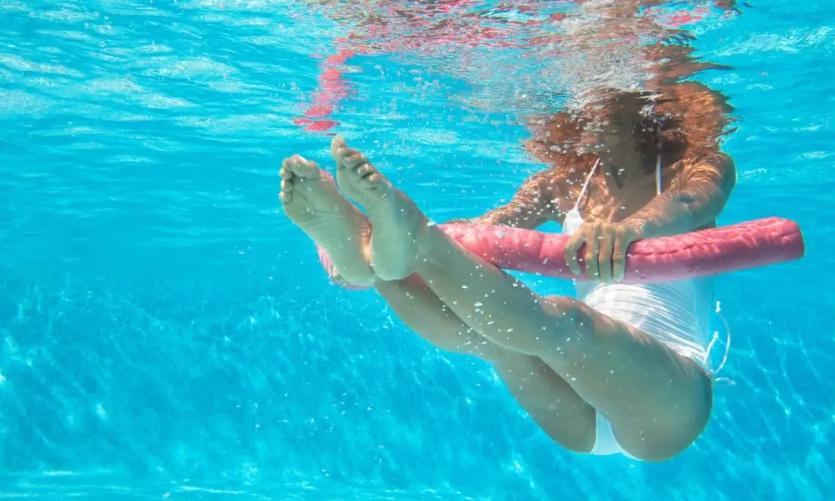 Donna esegue esercizi gambe piscina con un galleggiante rosa.