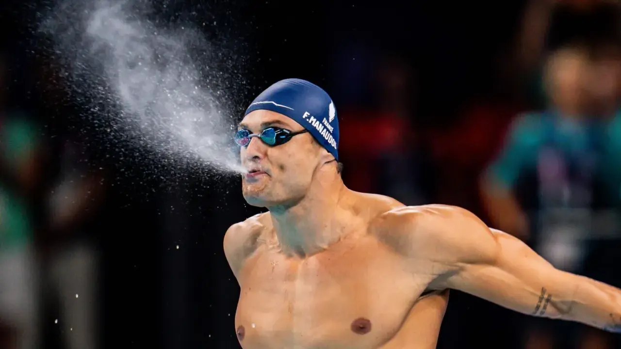 Florent Manaudou, nuotatore francese, spruzza acqua dalla bocca dopo una gara, con la cuffia blu e gli occhialini da nuoto.