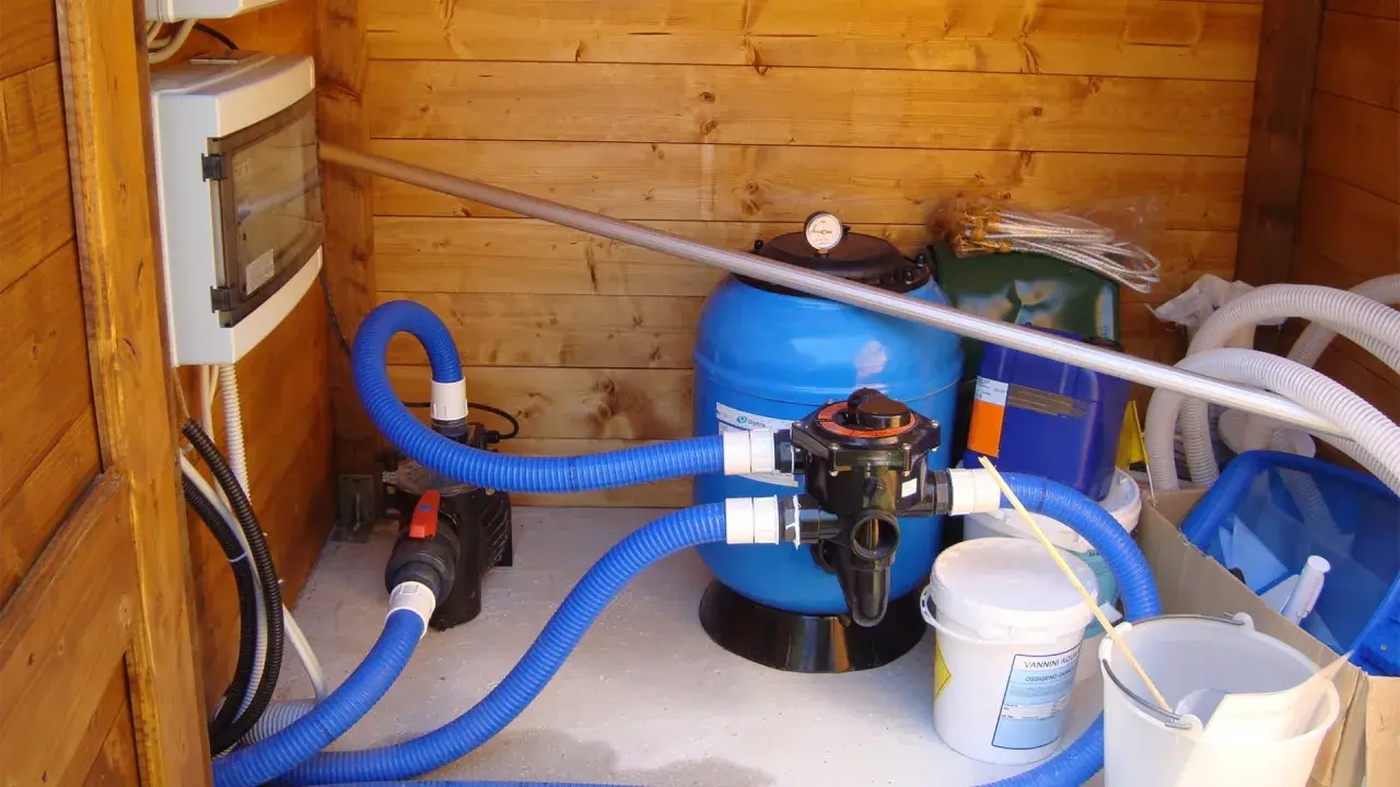 Sistema di filtrazione per piscina con filtro a sabbia, pompa e tubi blu. Il filtro a sabbia è il cuore del sistema per mantenere l'acqua pulita.