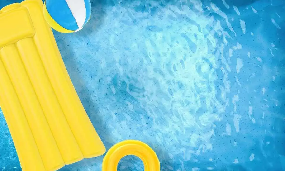 Un materassino giallo, una palla e un salvagente galleggiano in una piscina azzurra. Ideale per scoprire come pulire piscina gonfiabile.