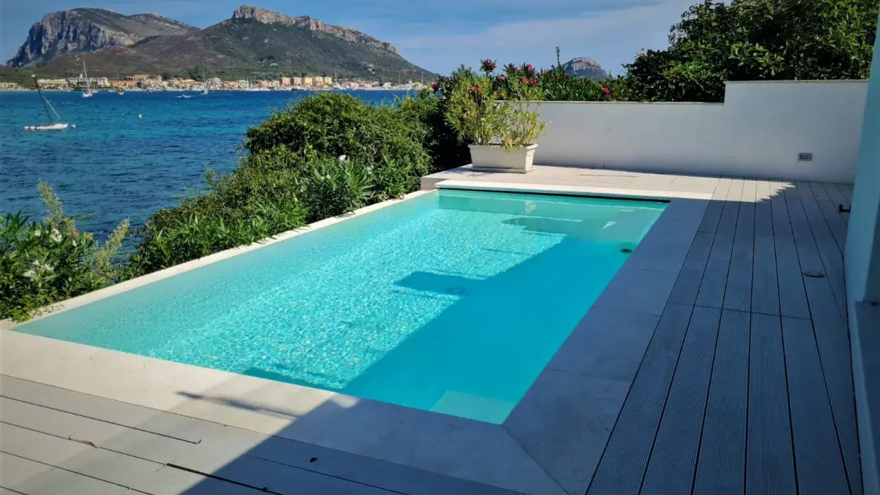 Piscina cristallina con vista mare. L'acqua, mantenuta con candeggina a un ph ideale, riflette il cielo azzurro e le montagne sullo sfondo.