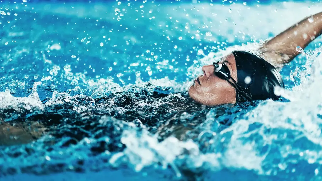 Atleta in nuoto dorso, godendo dei benefici di questo sport. L'acqua schizza intorno al suo viso concentrato.