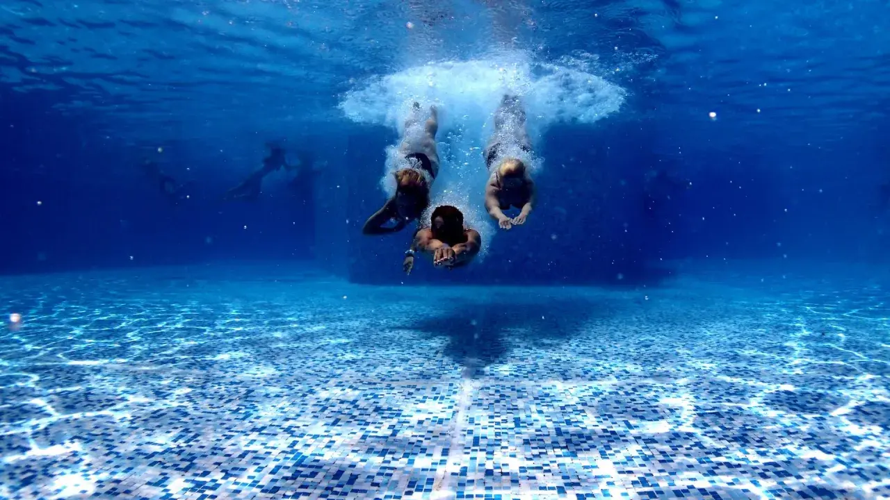 Subacquea, tre persone si tuffano in piscina. Chissà in quanto tempo un adulto impara a nuotare, ma loro sembrano già a loro agio.