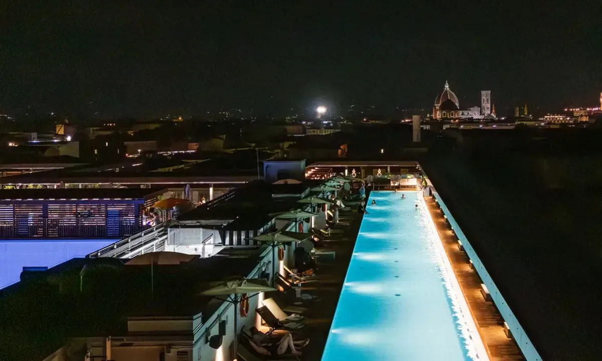 Una splendida piscina di sera, illuminata da luci soffuse, con la silhouette di Firenze sullo sfondo.