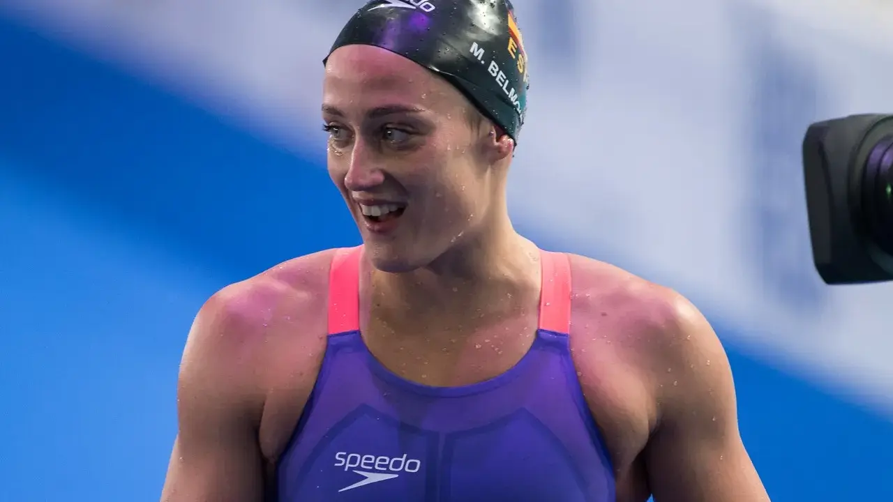 Mireia Belmonte, bagnata e sorridente, indossa un costume da nuoto viola e una cuffia nera.