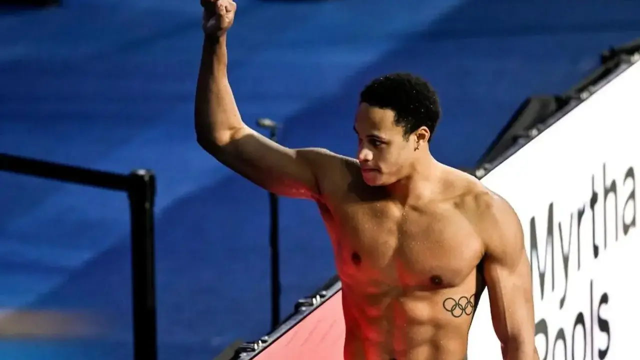 Shane Tusup, nuotatore con un pugno alzato, celebra una vittoria. Sul suo petto, i cinque cerchi olimpici.