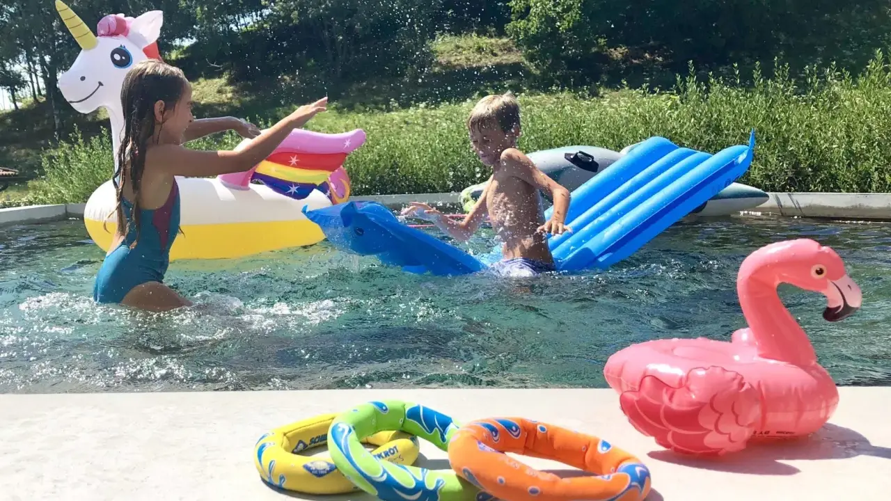 Bambini si divertono in piscina con gonfiabili colorati, tra cui un unicorno e un fenicottero. Perfetti giochi da fare in piscina senza niente per un'estate indimenticabile.