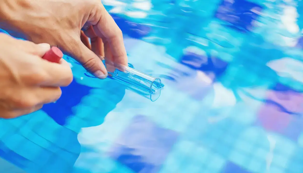 Mano che preleva campione d'acqua piscina con provetta. Il cloro basso indica necessità di trattamento.