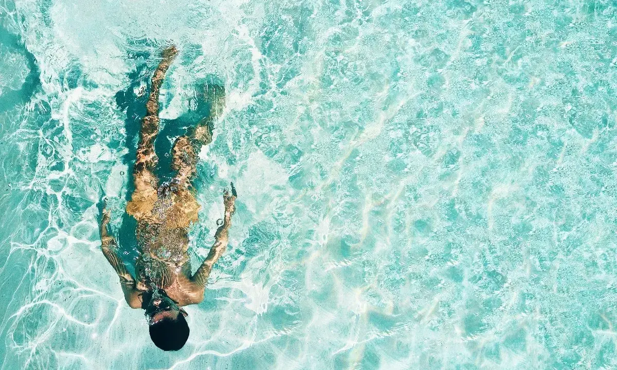 Persona sott'acqua in piscina, con riflessi luminosi. Chissà se il suo tatuaggio è fresco, dopo quanto tempo in piscina?