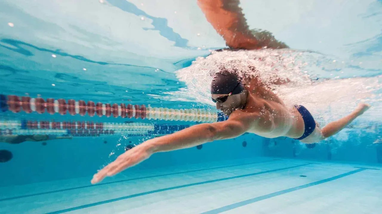 Nuotatore in azione, un'ottima dimostrazione che il nuoto fa dimagrire. L'acqua cristallina della piscina riflette la sua determinazione.