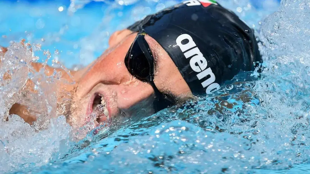 Nuotatore con cuffia Arena e occhialini, immerso nell'acqua con spruzzi. Potrebbe essere Pasquale Giordano in azione.