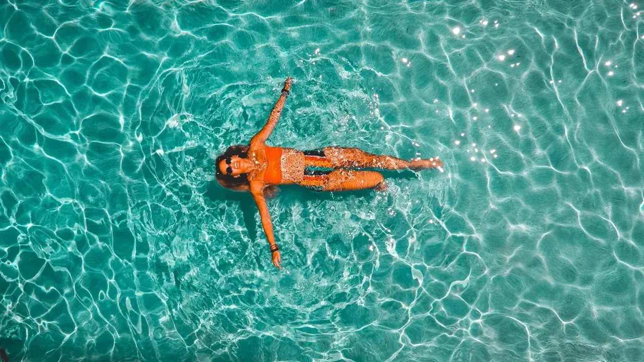Donna rilassata galleggia in piscina. Il nuoto è un ottimo modo per migliorare la forma fisica, con risultati visibili nel nuoto cellulite prima e dopo.