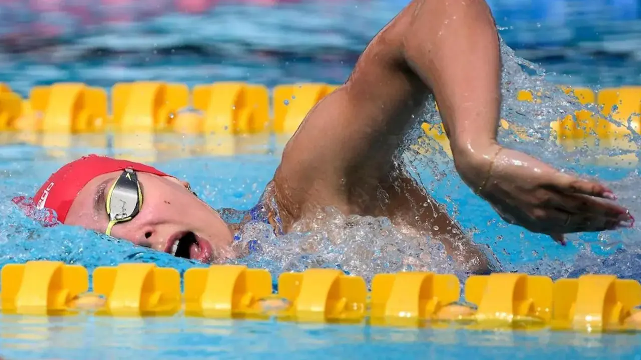 Nuotatrice con cuffia rossa e occhialini, in azione in piscina. Camille Muffat, un'atleta determinata.