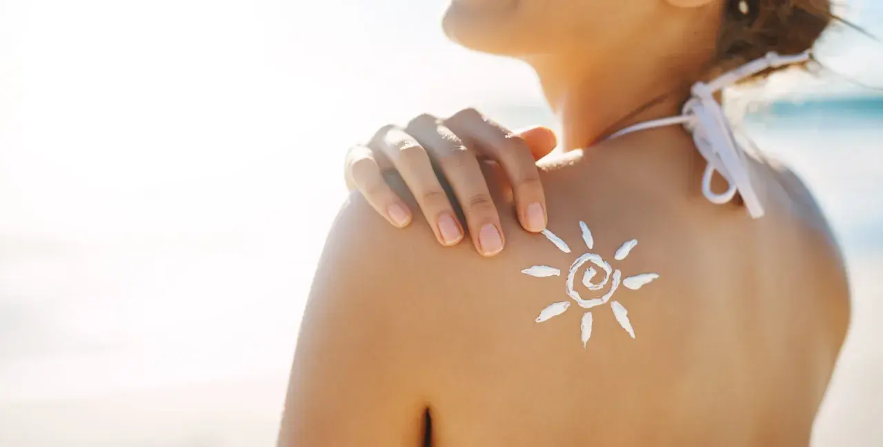 Sole sulla pelle, ma attenzione: il cloro toglie l'abbronzatura. Crema solare a forma di sole sulla spalla di una donna in spiaggia.