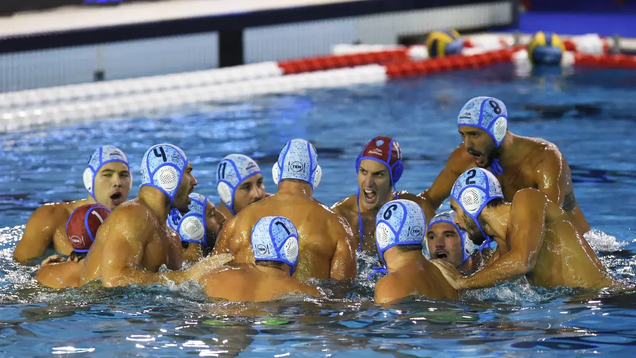 Giocatori di pallanuoto in acqua, con cuffie numerate, in un momento di intensa competizione. I loro ruoli pallanuoto sono evidenti dalla loro posizione e dall'azione.