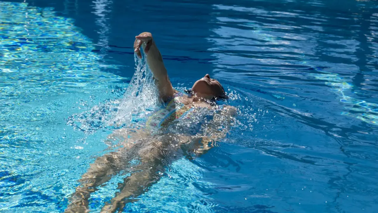 Donna nuota a dorso in una piscina olimpionica, godendosi la profondità e la frescura dell'acqua cristallina.