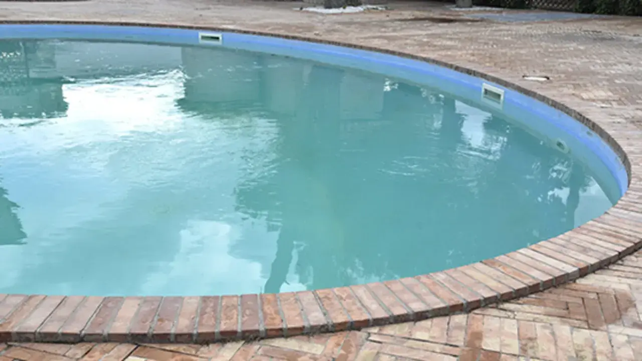 Piscina con acqua torbida e riflessi del cielo, circondata da un bordo in mattoni.