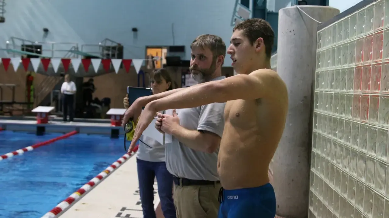 Nuotatore pronto a gareggiare, forse Matt Grevers, con allenatori al bordo piscina.