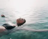 Donna galleggia sull'acqua, superando la paura di nuotare dove non si tocca. La luce del sole illumina il suo viso sereno.