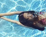 Ragazza nuota sott'acqua, capelli scuri fluttuano. Le bollicine d'aria evidenziano gli effetti del cloro sui capelli.