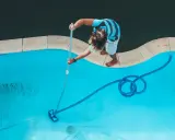 Ragazzo pulisce la piscina con un aspirafango piscina fai da te, rimuovendo detriti dal fondo azzurro.