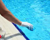 Persona con guanto bianco immerge un oggetto blu in piscina. Il cloro a cosa serve? A mantenere l'acqua pulita e sicura per nuotare.