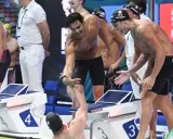 Atleti italiani festeggiano dopo la staffetta 4x100. Un nuotatore porge la mano a un compagno, gioia e sudore bagnano la corsia.