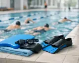 Attrezzatura da nuoto: cuffia, occhialini, tavoletta, pinne e asciugamano, pronti per il programma nuoto in piscina con nuotatori sullo sfondo.
