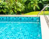 Piscina fuori terra con piastrelle blu scintillanti e vegetazione lussureggiante. La manutenzione piscina fuori terra è fondamentale per godersi questo angolo di paradiso.