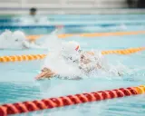 Nuotatore in azione, concentrato su come nuotare più veloce. Schizzi d'acqua e bracciate potenti in piscina.