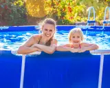 Donna e bambina sorridono in piscina. L'acqua limpida, forse trattata con bicarbonato, riflette il sole.