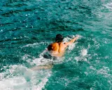 Uomo con schiena muscolosa nuotare in mare aperto, circondato da spruzzi d'acqua cristallina.