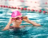 Donna con cuffia e occhialini rosa in piscina, pronta a godere dei benefici piscina.