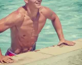 Uomo sorridente emerge dall'acqua cristallina, con spalle possenti che dimostrano come il nuoto allarga le spalle.