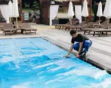 Uomo in blu sistema il telo in pvc della piscina, un passo fondamentale per capire come pulire il telo in pvc della piscina e mantenerla splendente.