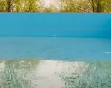 La piscina in inverno va svuotata. L'acqua residua riflette il verde degli alberi e il cielo, mentre il fondo mostra i segni del tempo.