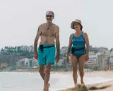 Coppia over 60 passeggia sulla spiaggia, un esempio di allenamento nuoto e vita attiva.