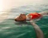 Donna galleggia serena in acqua cristallina, pensando ai rimedi per l'otite del nuotatore.