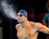 Florent Manaudou, nuotatore francese, spruzza acqua dalla bocca dopo una gara, con la cuffia blu e gli occhialini da nuoto.