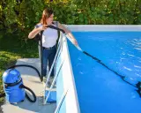 Donna pulisce la piscina con un aspiratore, preparandola per la riapertura dopo l'inverno.