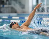 Atleta in piscina esegue la nuotata a **scheda dorso**, con il braccio destro sollevato e l'acqua che schizza.